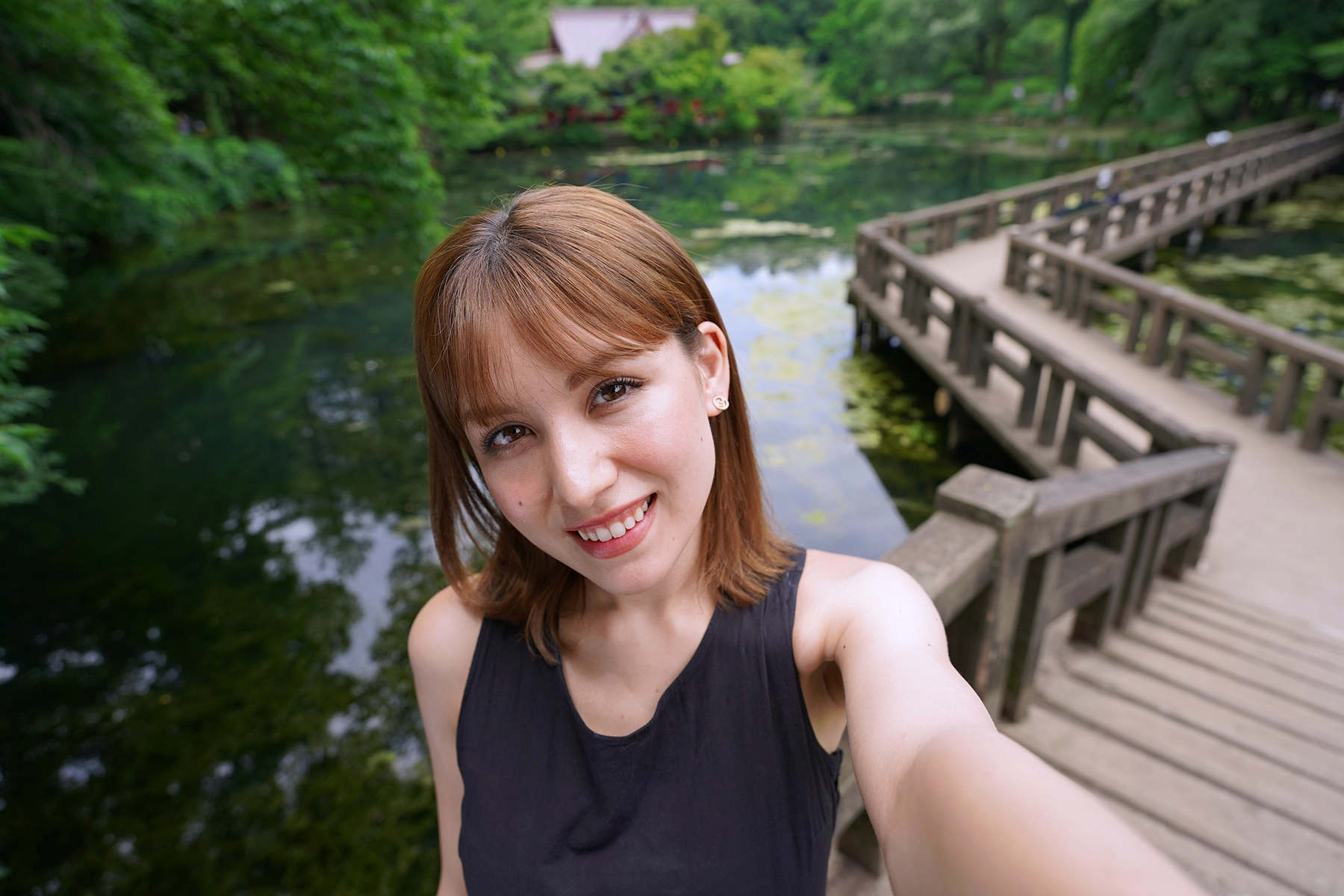 Mulher tirando uma selfie enquanto faz um vlog com uma câmera sem espelho em uma ponte de madeira sobre um lago.