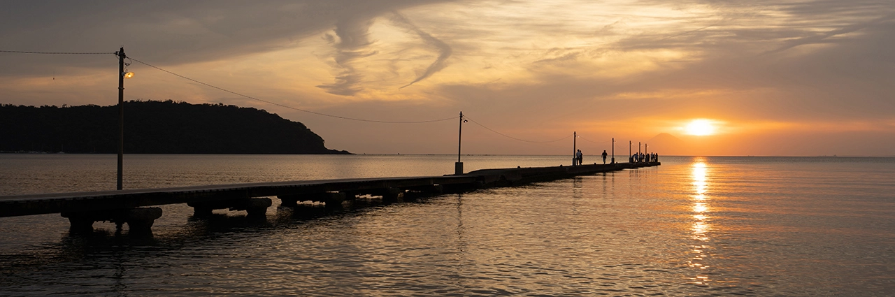 Puesta de sol dorada sobre un mar en calma con siluetas en un muelle, capturada durante la revisión del Tamron 16-30 mm F2,8 G2, que muestra el contraste dinámico y la claridad de borde a borde en gran angular.