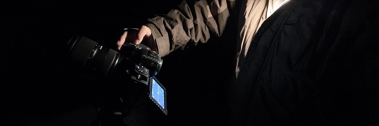 Photographer using Astro Focus Lock on TAMRON Lens Utility™ at night to achieve precise focus during astrophotography session in low-light conditions
