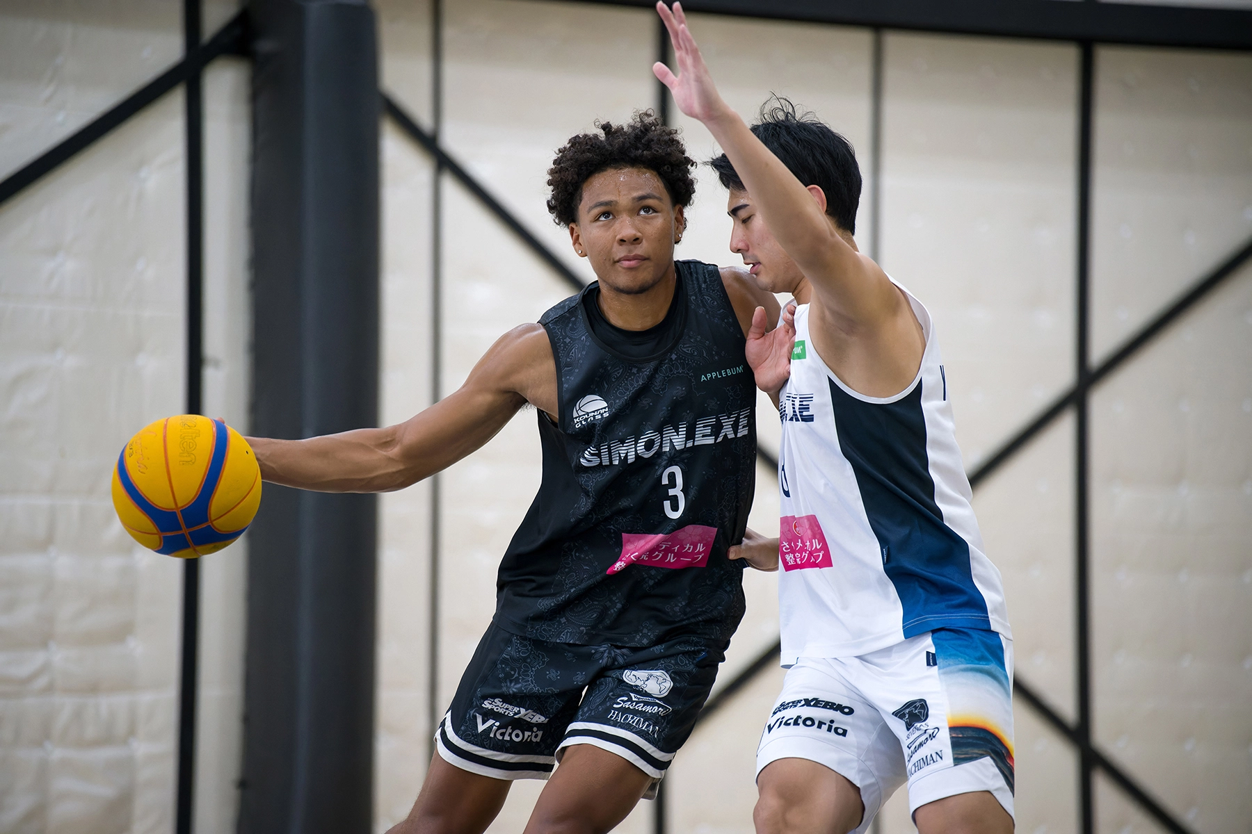 Dos jugadores de baloncesto en una intensa acción de uno contra uno durante un partido 3x3 en pista cubierta, mostrando la concentración y el movimiento atléticos: un ejemplo de fotografía deportiva dinámica que capta la competición en tiempo real.