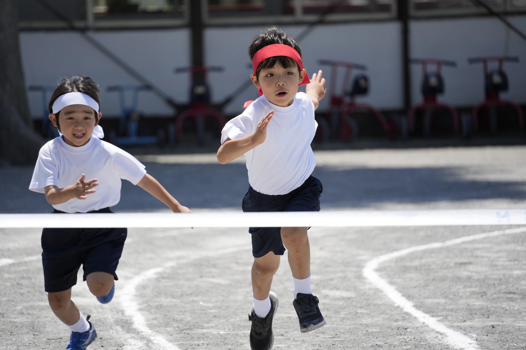 Dos niños corren hacia la línea de meta durante una carrera deportiva escolar, capturados a mitad de camino con caras expresivas y un movimiento nítido: un atractivo ejemplo de fotografía deportiva dinámica.