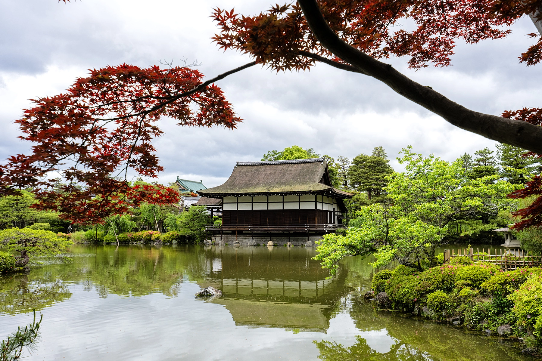 Un temple entouré d'arbres verts avec un arbre à feuilles rouges au premier plan