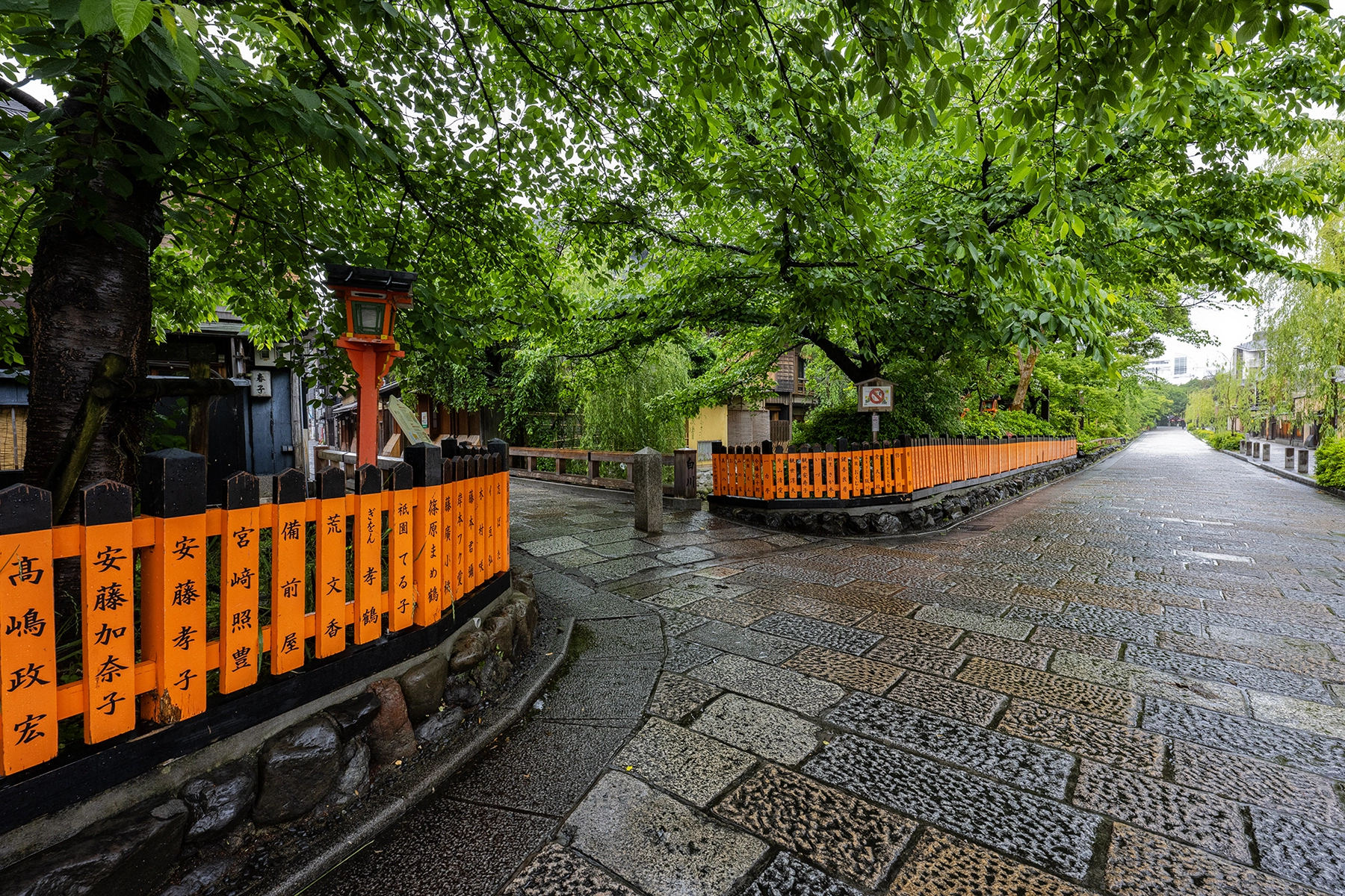 Une allée en pierre avec des clôtures noires et orange et des arbres verts.