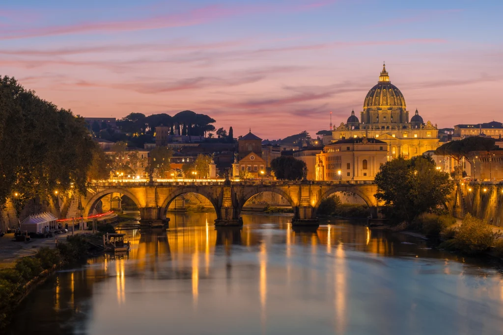 The St. Angelo Bridge in Rome with St Peter's Basilica in the background at sunset.