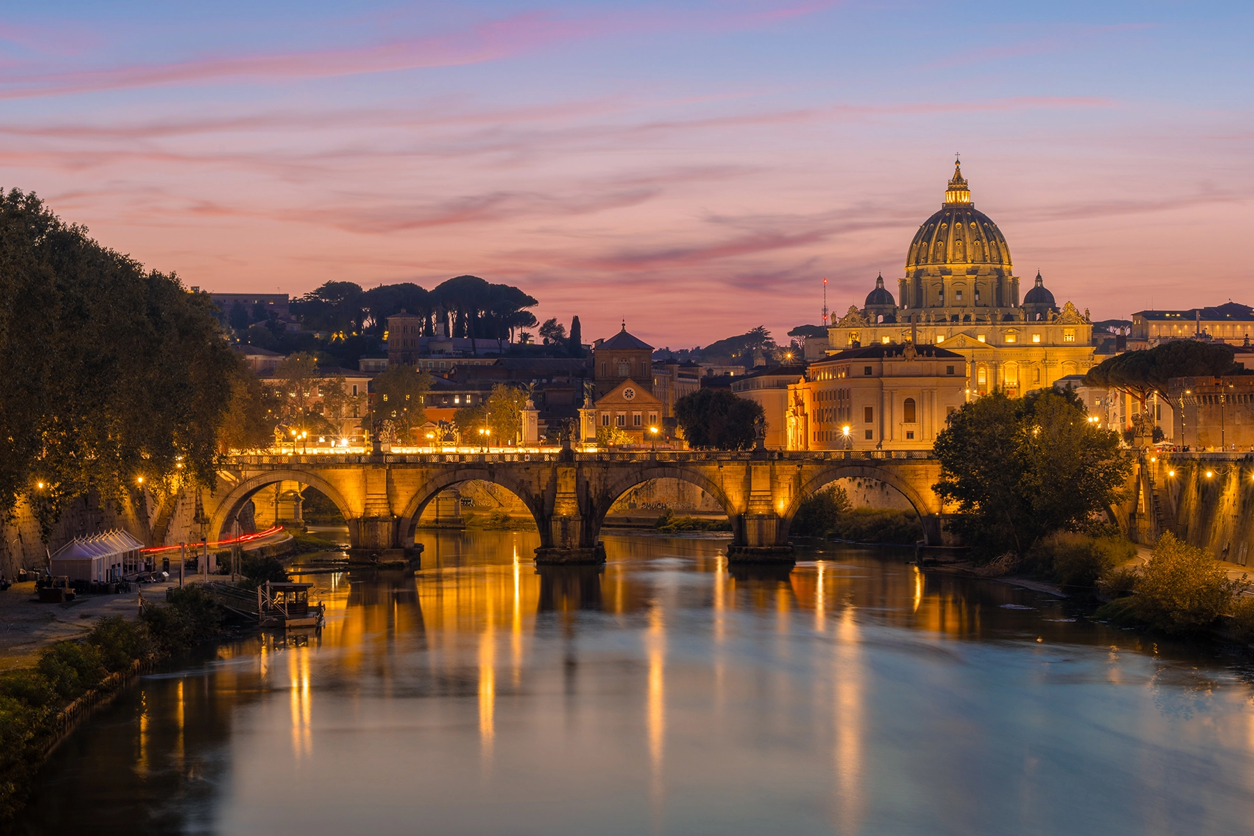 The St. Angelo Bridge in Rome with St Peter's Basilica in the background at sunset.