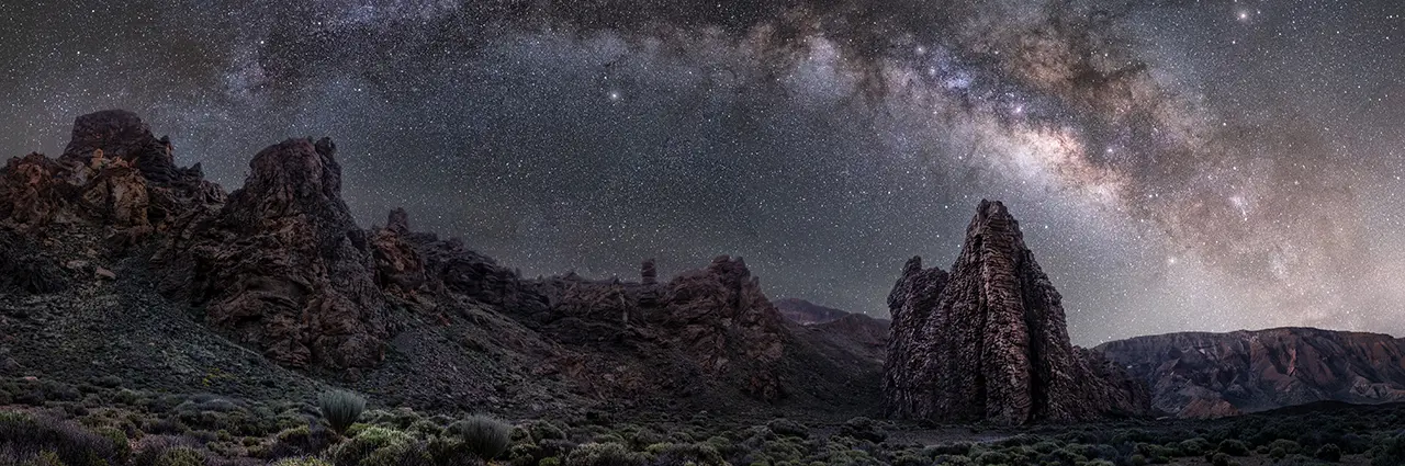 Via Láctea estendendo-se pelo céu noturno acima de formações rochosas escarpadas, capturada com uma lente grande angular Tamron f/2.8 - mostrando os detalhes possíveis com a melhor lente para astrofotografia e cenas com pouca luz.