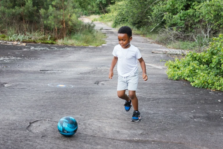 A young boy kicking a soccer ball in the dark sand.