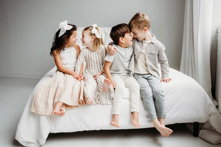 Four young children sitting together on a bed, smiling and interacting with each other