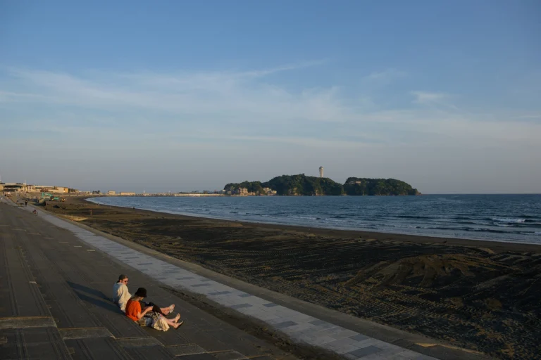 Two people sitting on concrete steps with a sand beach and water in front of them.