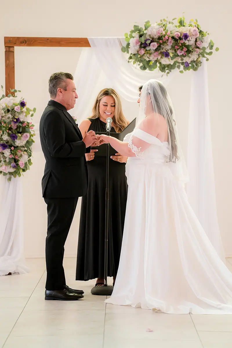 La novia y el novio intercambiando anillos durante su ceremonia de boda, captada con tonos suaves y naturales y una nítida claridad, lo que demuestra que el mejor objetivo para fotografía y vídeo está en acción.