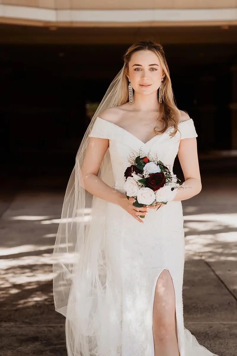 Novia con un vestido de novia blanco sujetando un ramo, captada con luz natural con detalles nítidos y un suave desenfoque del fondo, para mostrar el mejor objetivo para foto y vídeo en fotografía de bodas.