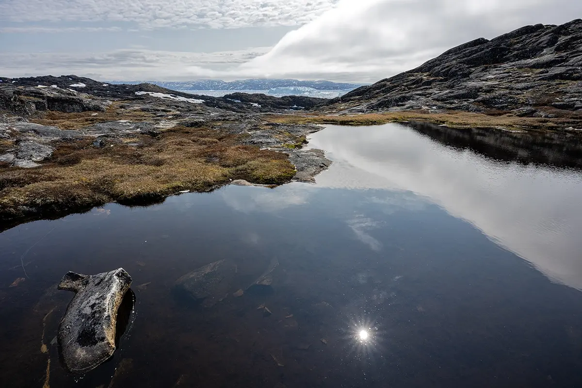 Arctic tundra landscape near Ilulissat, Greenland, with reflective water pool and rocky terrain captured using a Tamron wide-angle lens