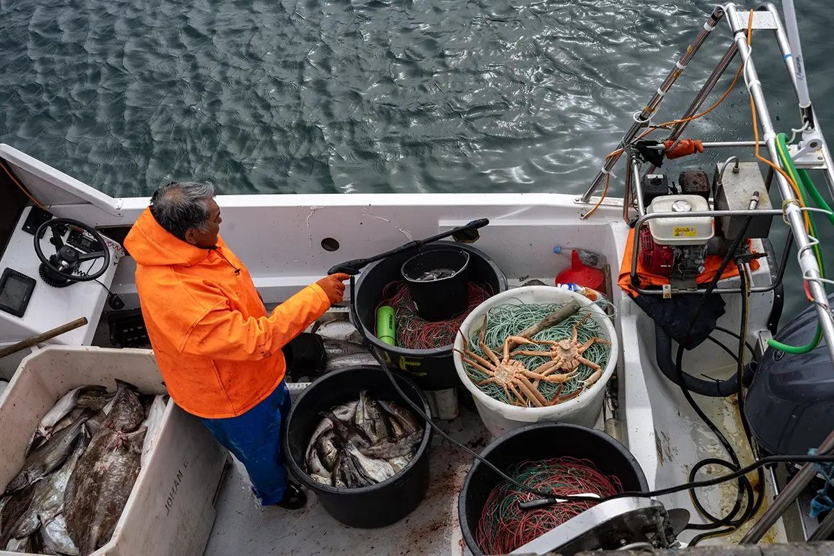 Greenlandic fisherman in bright orange jacket on a boat with freshly caught fish, crab, and nets, photographed with a Tamron lens in Disko Bay