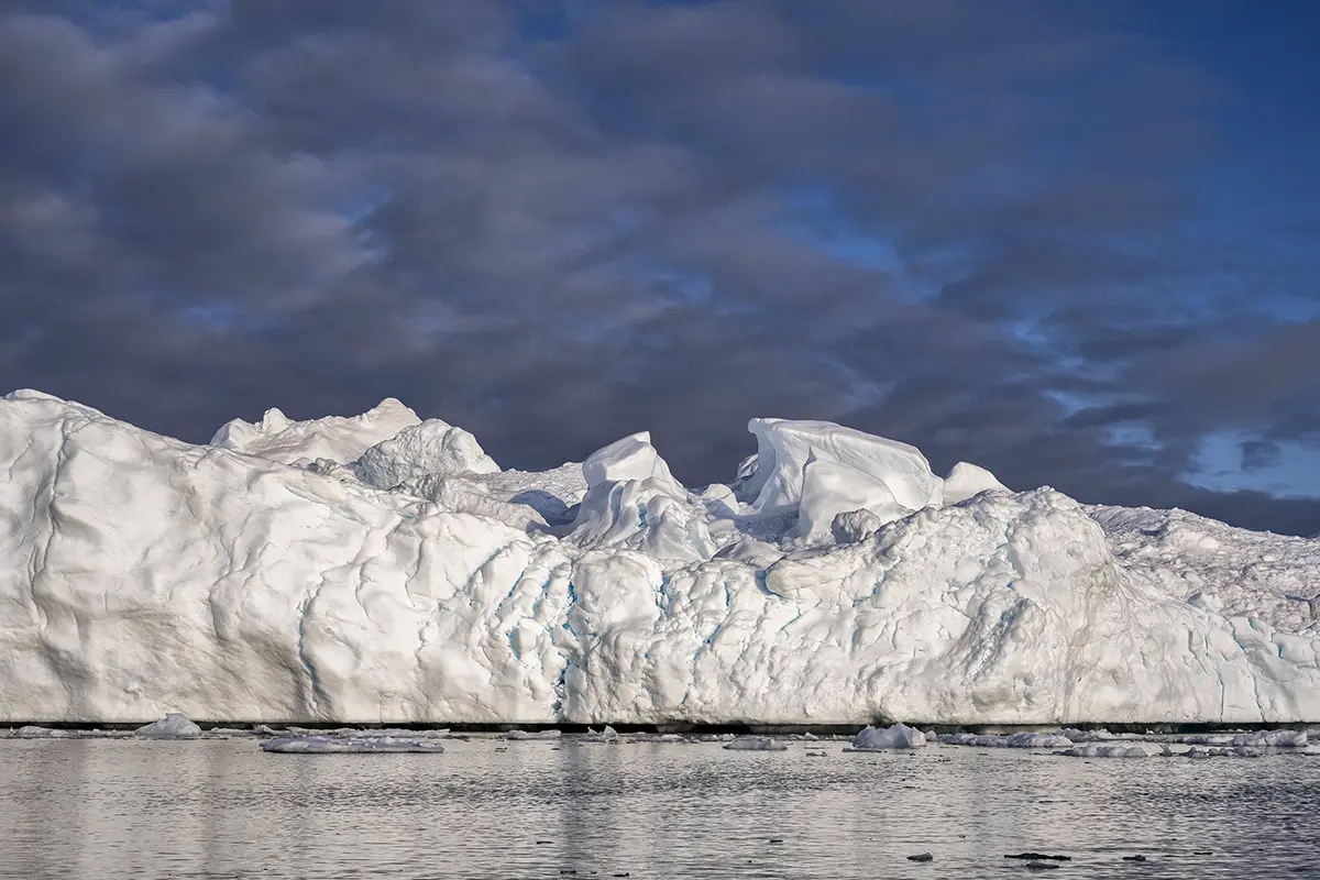 Towering iceberg in Disko Bay, Greenland, with blue cracks and textures highlighted by Arctic light, photographed with a Tamron telephoto lens