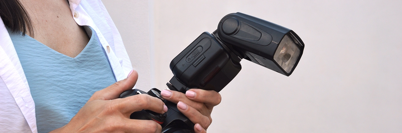 Mujer sujetando una cámara con un flash externo montado.