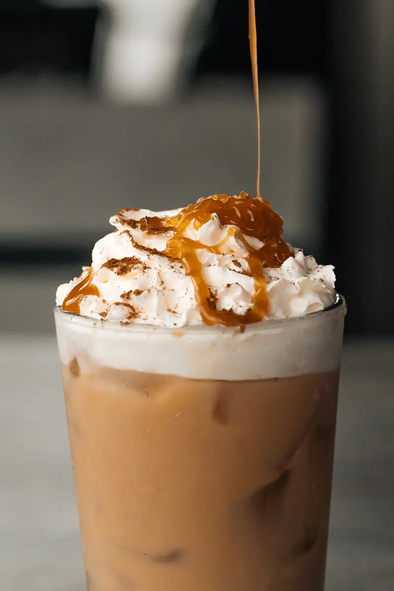 Café con leche helado de otoño con nata montada, canela y llovizna de caramelo, diseñado para la fotografía de alimentos y bebidas de otoño.
