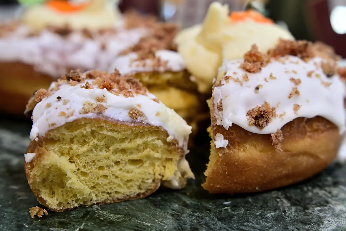 Primer plano de donuts otoñales helados con cobertura desmenuzada, colocados sobre una superficie rústica para fotografía de alimentos y bebidas otoñales.