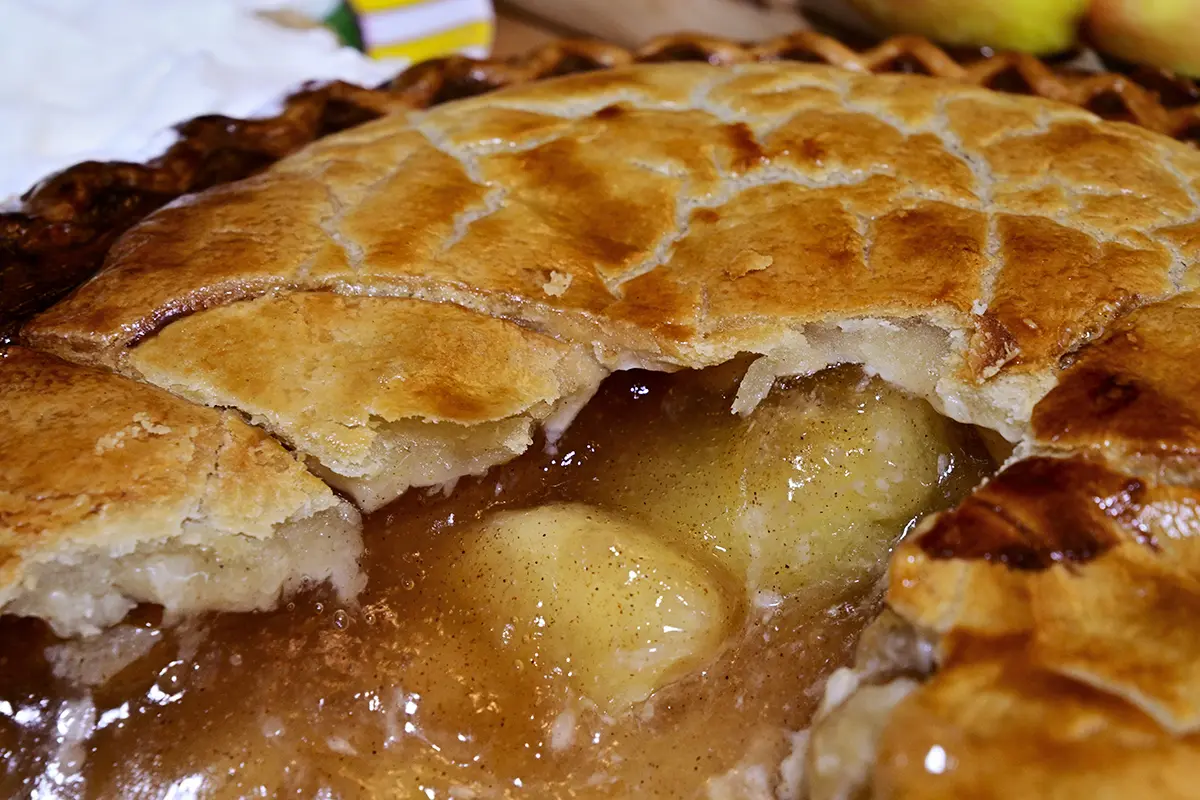 Primer plano de una tarta de manzana dorada con una corteza hojaldrada y un relleno caliente de manzana con especias y canela.