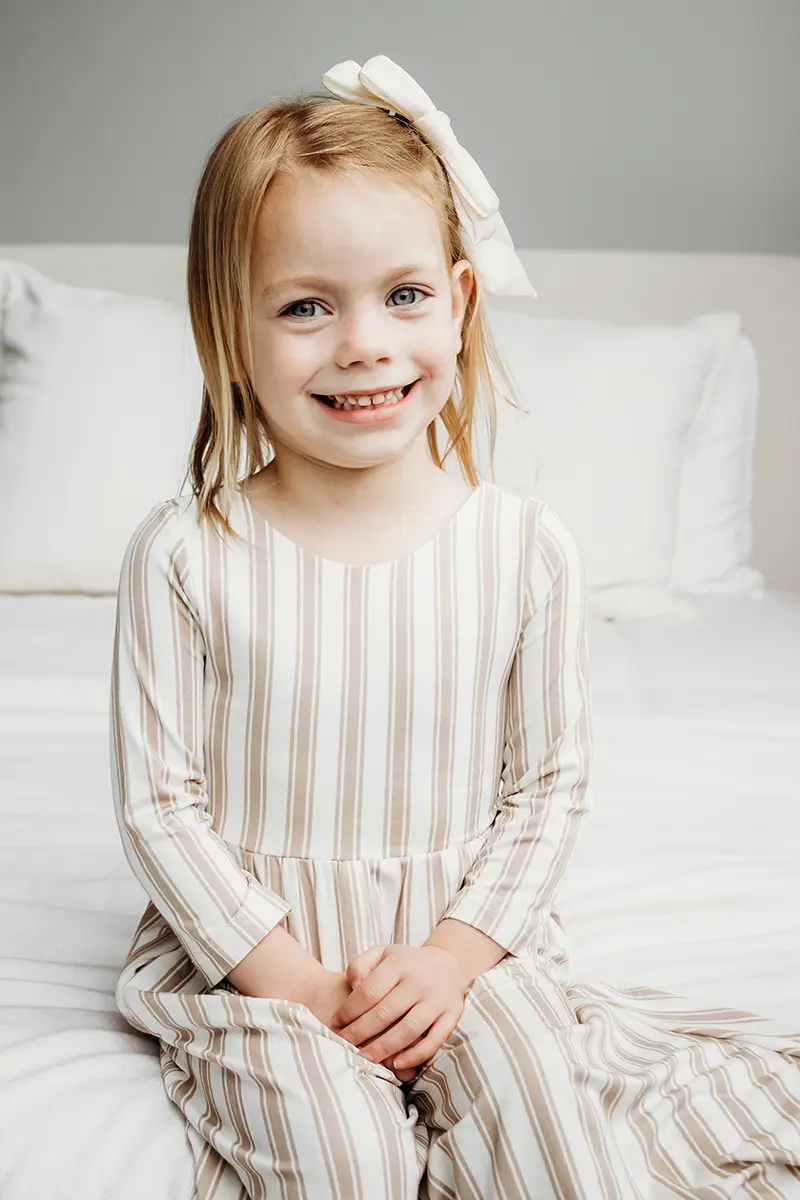 Menina em um vestido listrado sorrindo durante uma sessão de retrato, mostrando um exemplo de lente prime versus zoom para fotografia de família.