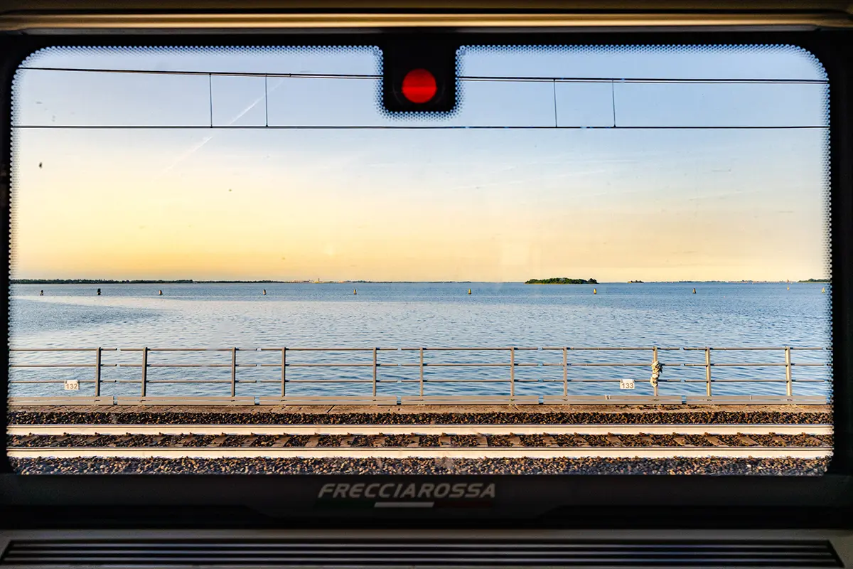 Vue de la lagune vénitienne depuis la fenêtre d'un train Frecciarossa, capturant l'approche de la ville flottante d'Italie pour ce guide de photographie de voyage de Venise.