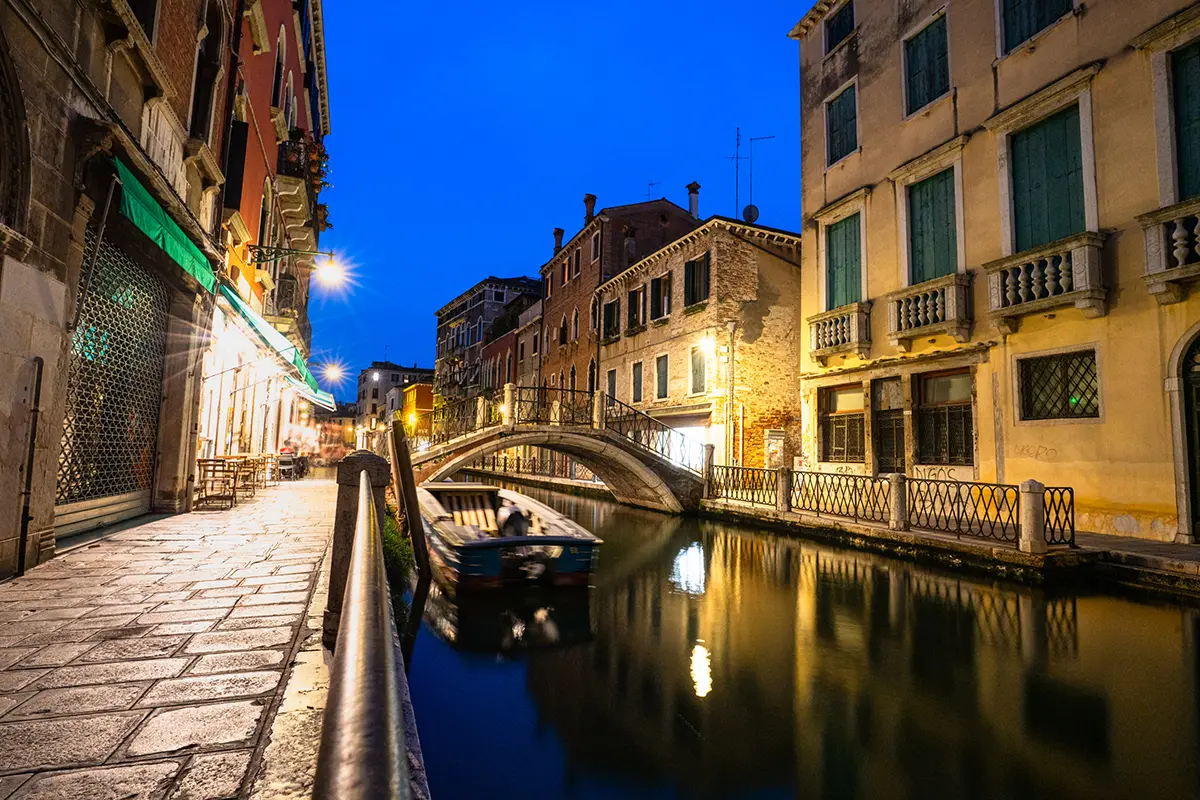 Photographie à l'heure bleue d'un canal vénitien avec des reflets et un pont en pierre, prise pour ce guide de photographie de voyage à Venise.
