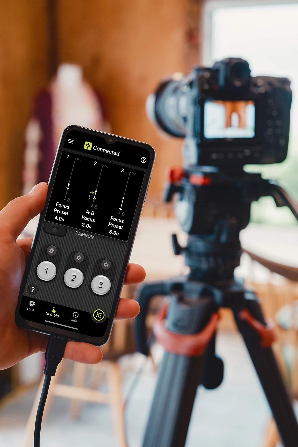 Smartphone controlando los preajustes de enfoque a través de TAMRON Lens Utility mientras graba vídeo con una cámara sin espejo montada en un trípode en un estudio.
