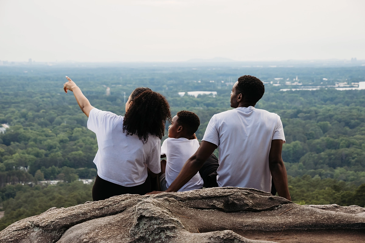 Família sentada em um parapeito de rocha com vista para uma paisagem cênica durante uma sessão de fotografia de família ao ar livre.