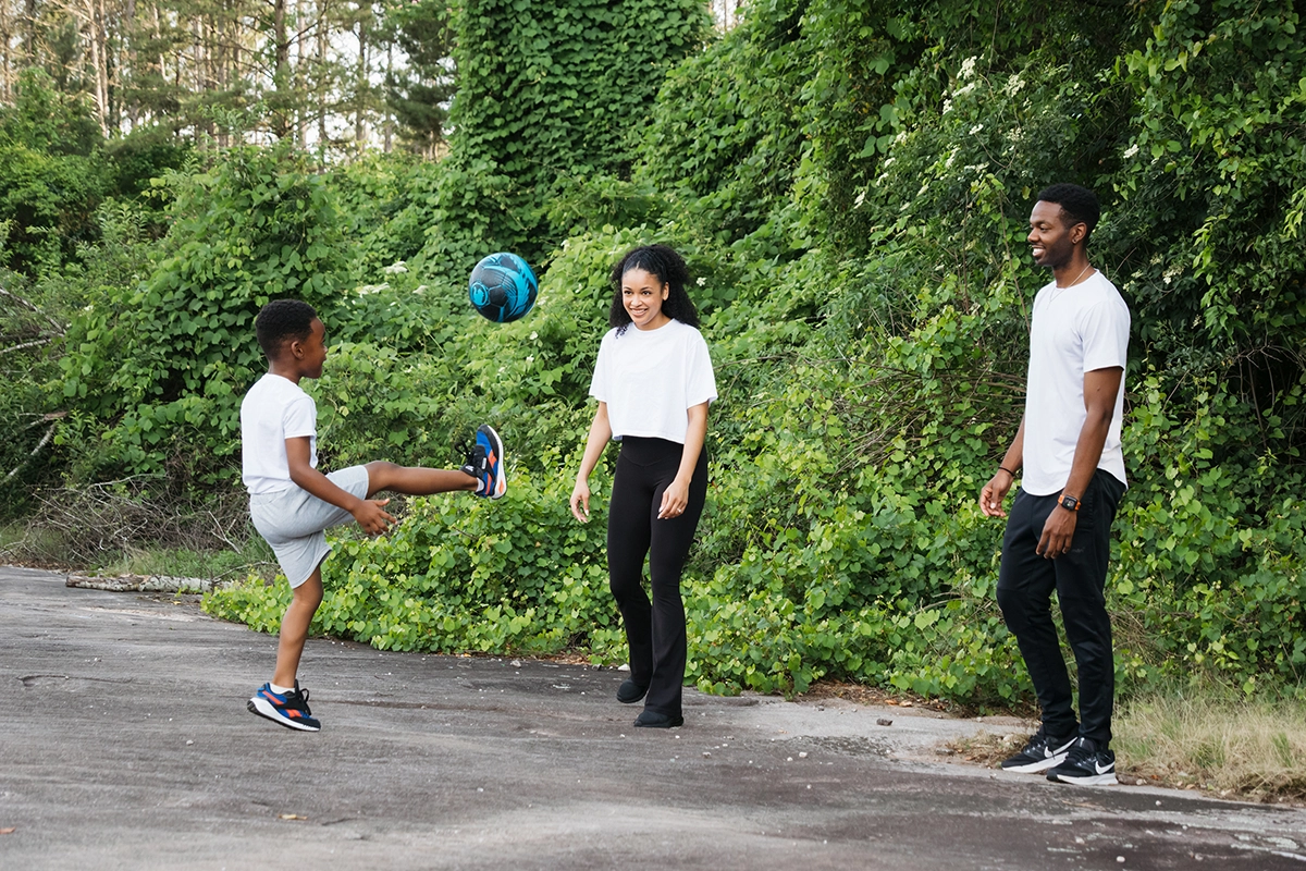 Família jogando futebol juntos ao ar livre durante uma sessão de fotografia de família espontânea.