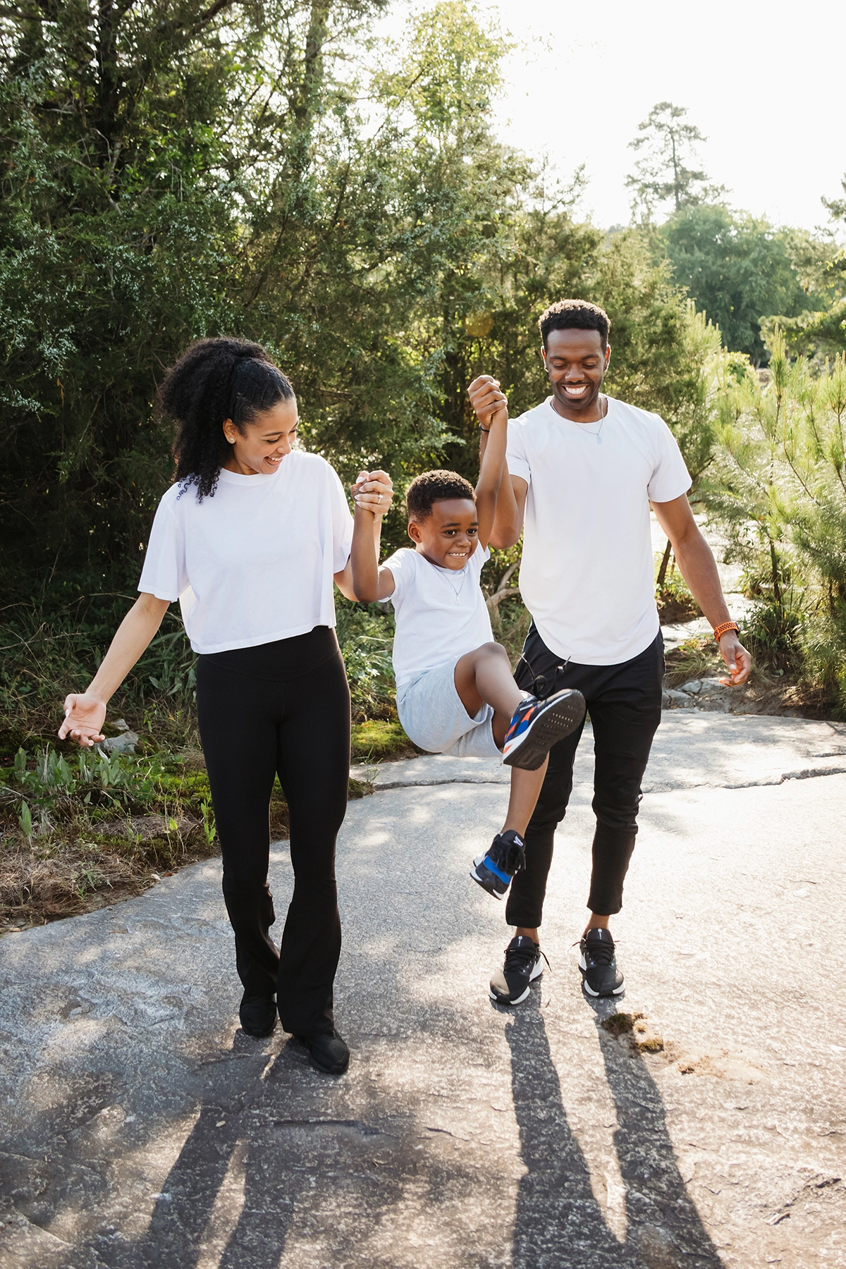Pais balançando seus filhos enquanto caminham ao ar livre durante uma sessão de fotografia de família espontânea.