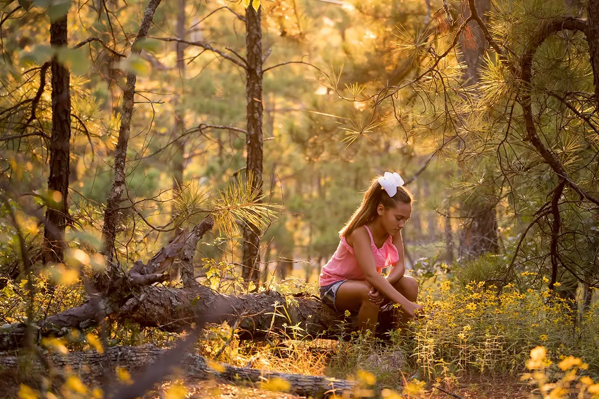 Retrato de menina na floresta com luz de fundo em fotografia da hora de ouro.