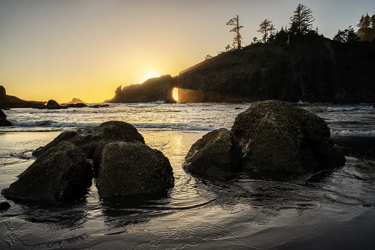 Pôr do sol na hora dourada em uma praia rochosa com falésias.