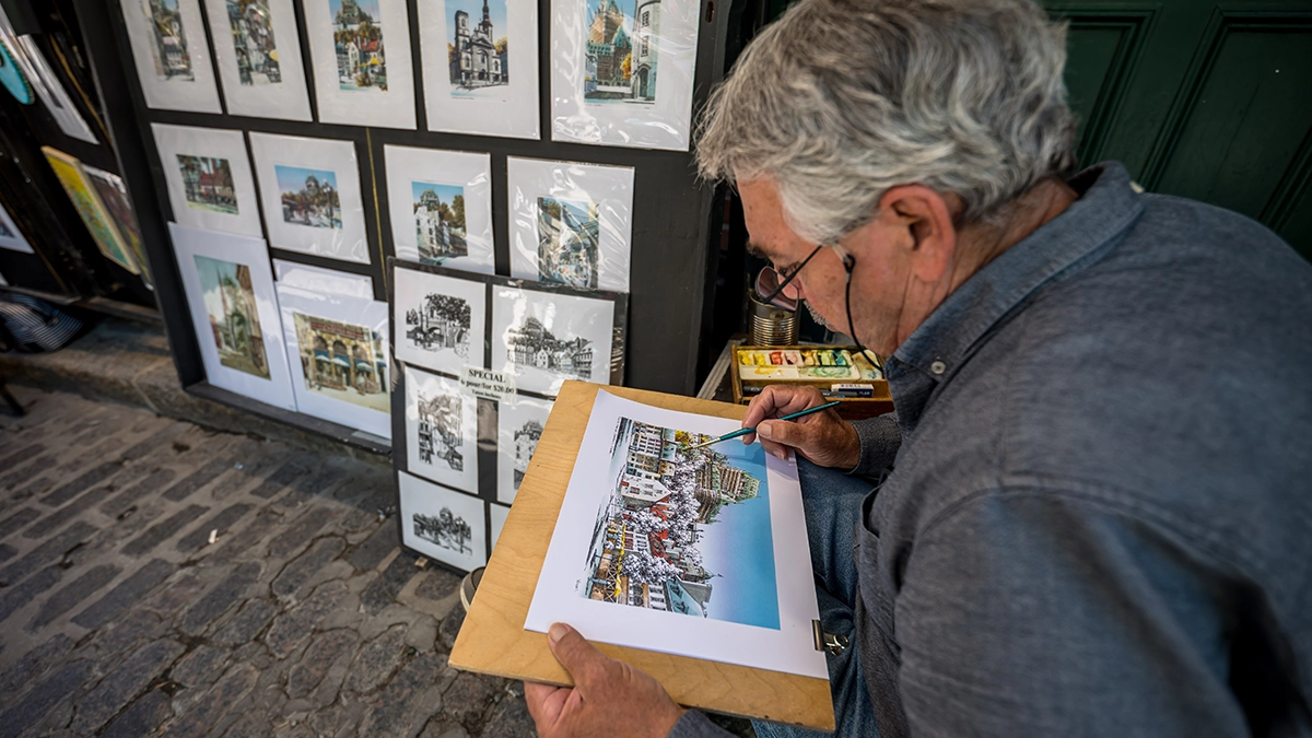 Artista callejero pintando en un callejón estrecho, fotografiado con el objetivo ultra gran angular Tamron 16-30 mm F/2,8 Di III VXD G2, que capta el detalle y la inmersión para la fotografía de viajes y arquitectura.