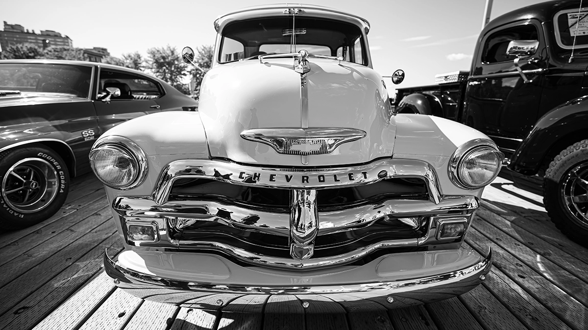 Fotografía en blanco y negro que muestra principalmente la parte delantera de una camioneta clásica Chevrolet 3100 aparcada sobre una superficie de madera. 