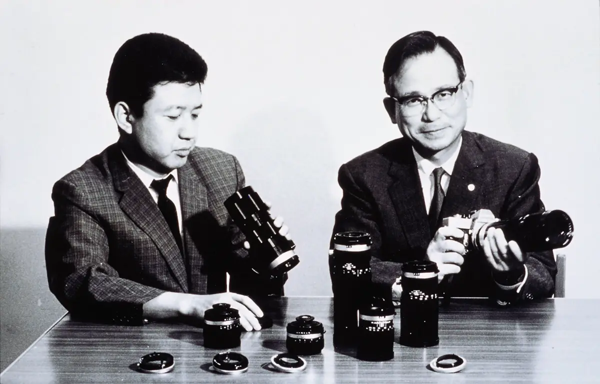 Tamron founders with early camera lenses, historic photo for the Tamron brand story.