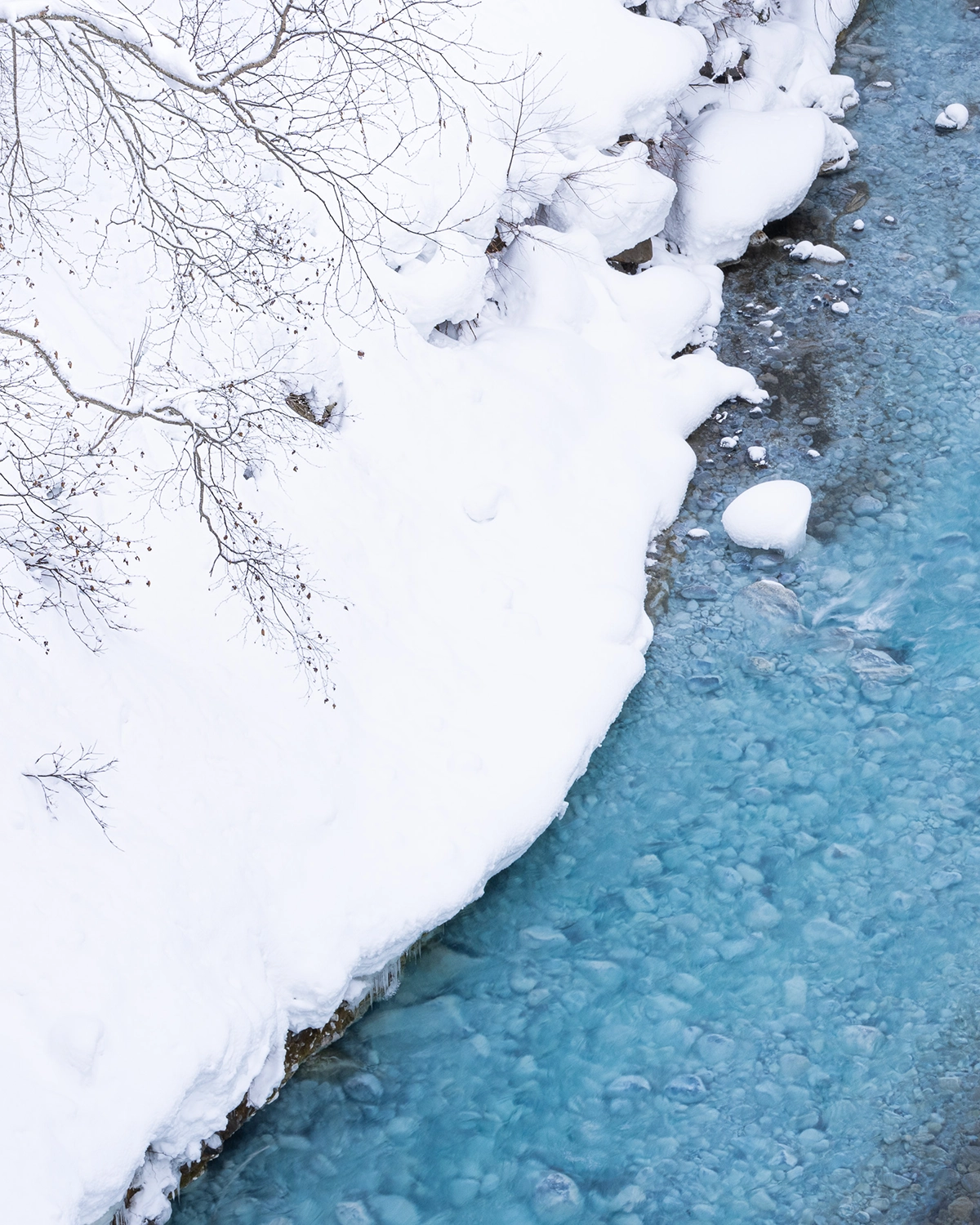Snow-covered riverbank and icy blue water in Hokkaido during winter