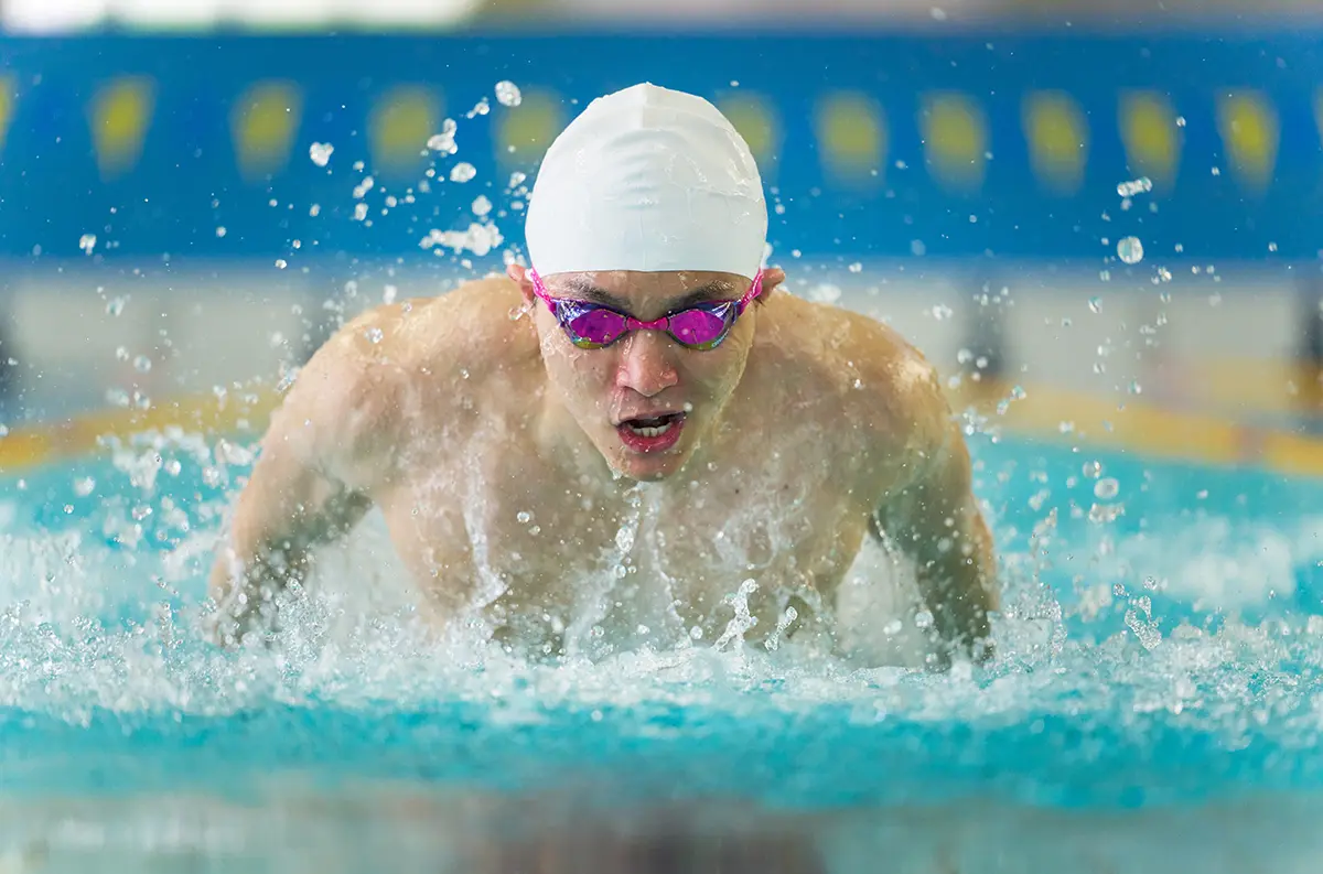 A man swimming in a pool with goggles on.