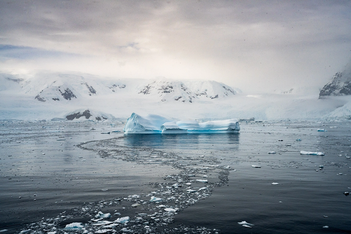 Iceberg floating among sea ice with snowy Antarctic mountains in the background during an Antarctica cruise photography expedition.