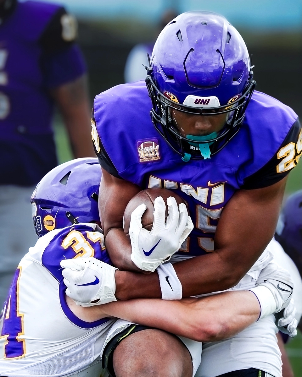 A football player carrying the football and getting tackled.