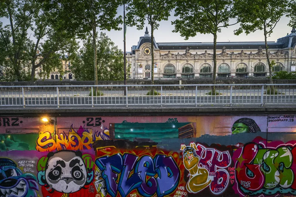 Un mur de graffitis colorés à Paris avec le musée d'Orsay en arrière-plan.