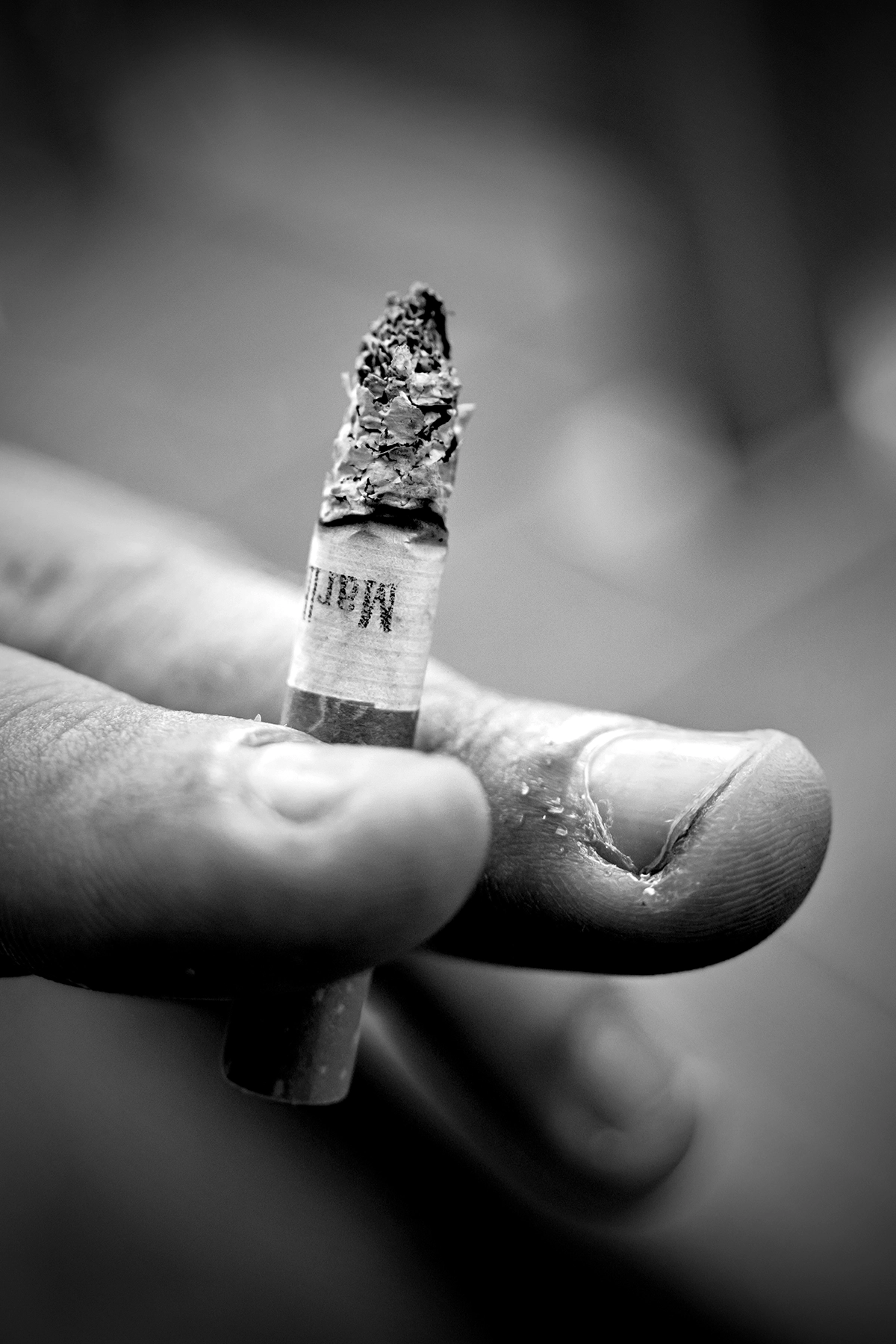Close-up black and white photo of a person holding a burning cigarette, illustrating mood, texture, and storytelling for photographers entering photo contests.
