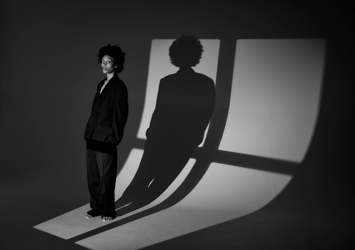 Black and white portrait of a woman standing barefoot in dramatic studio lighting with a bold shadow, illustrating creative use of light and form for photographers entering photo contests.