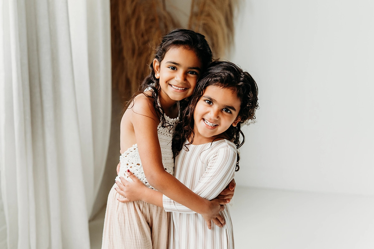 Two young sisters hugging and smiling in soft natural light, capturing warmth and emotion—an ideal example for photographers entering photo contests.