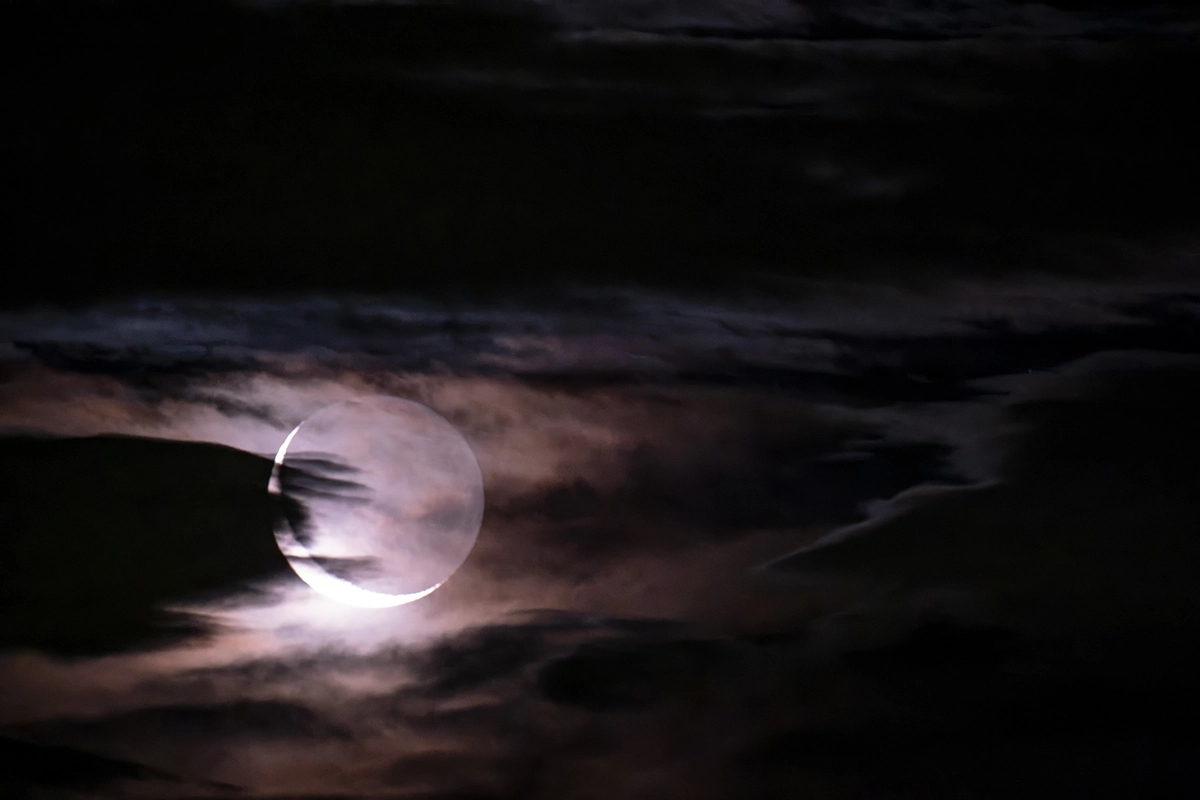 Crescent Oboroizuki moon glowing through dark clouds in a hazy night sky.