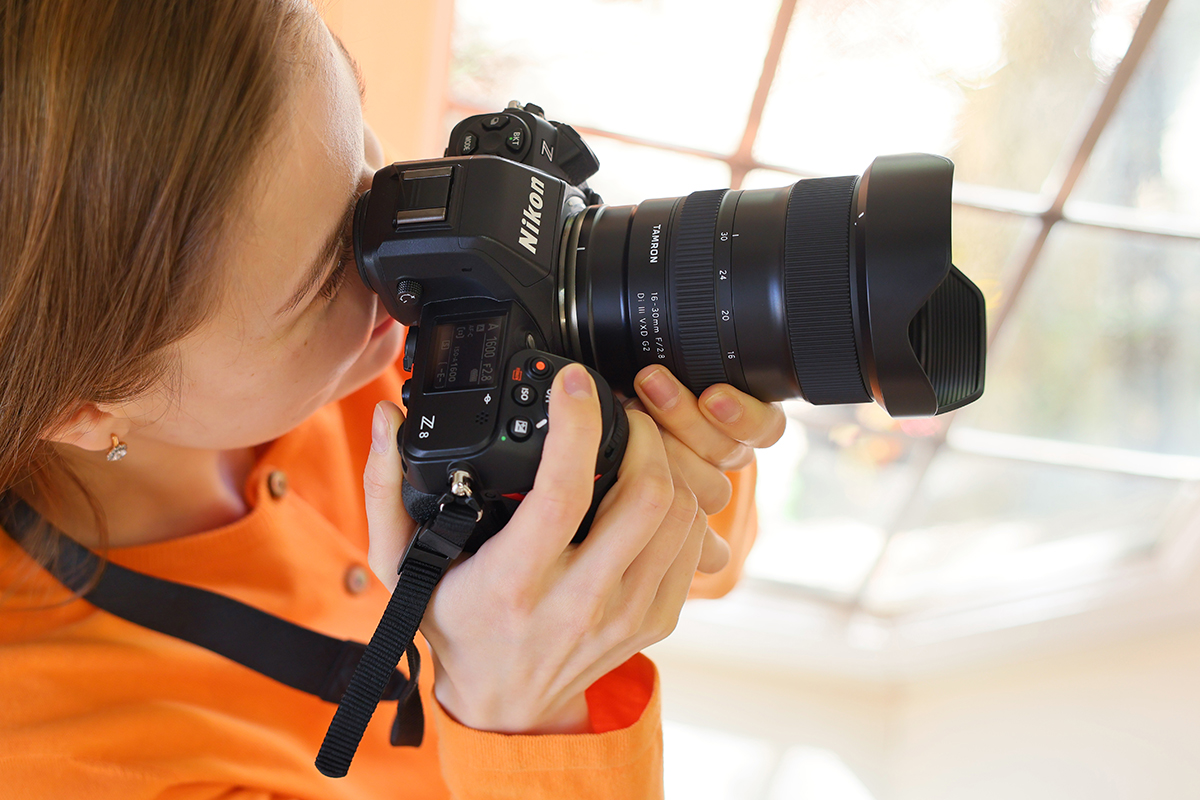 Fotógrafo con camisa naranja que utiliza una cámara Nikon Z8 con un objetivo Tamron 16-30 mm F2,8, capturando una escena de interior con luz natural de ventana, mostrando la versatilidad y claridad del gran angular.