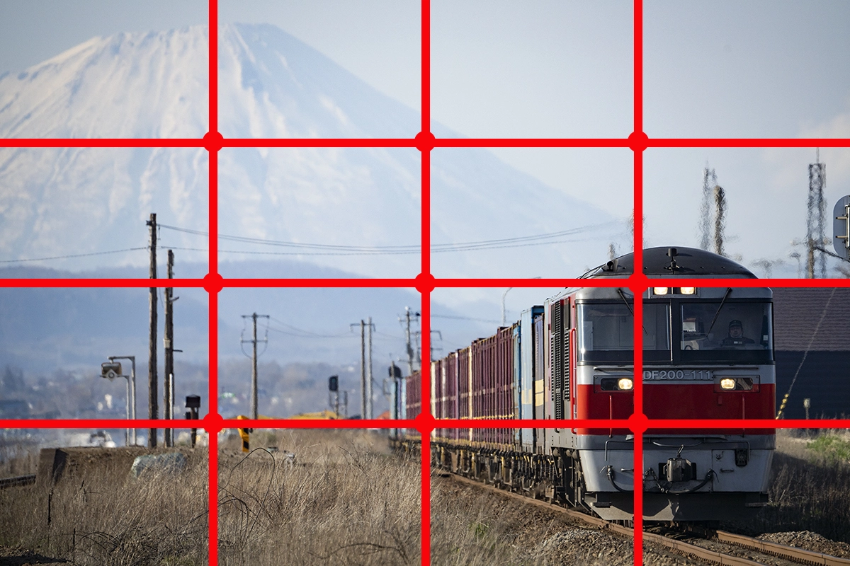 Train de marchandises avec une montagne en arrière-plan, superposé à une grille de règle de quart rouge pour illustrer la composition.
