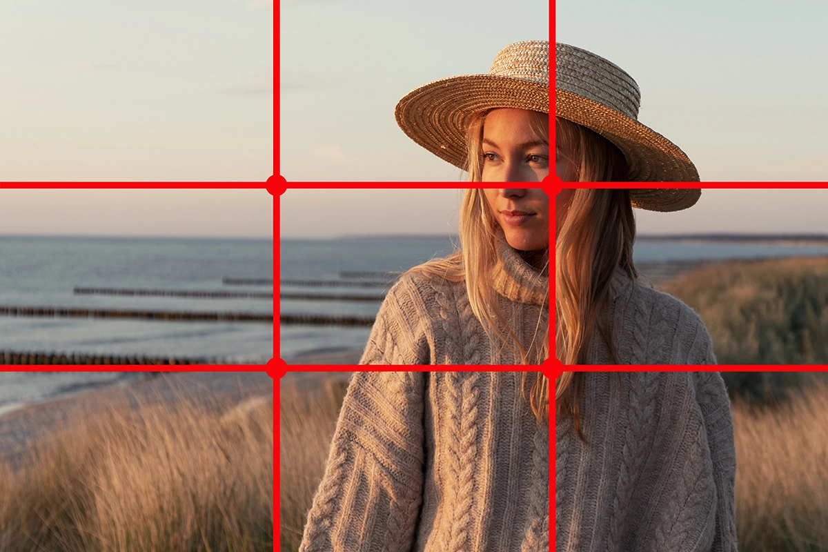 Portrait d'une femme sur la plage portant un chapeau, avec une grille rouge de la règle des tiers en surimpression démontrant la composition.