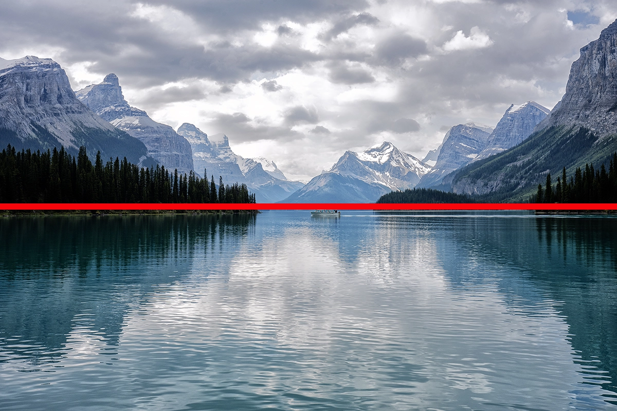 Lac de montagne avec des reflets de pics et d'arbres, divisé par une ligne horizontale rouge pour démontrer la symétrie de la composition.
