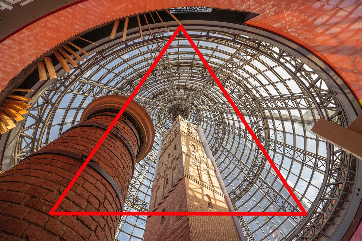 Vue vers le haut d'une tour en briques encadrée par un plafond en dôme de verre avec un triangle rouge en surimpression, démontrant une composition triangulaire.