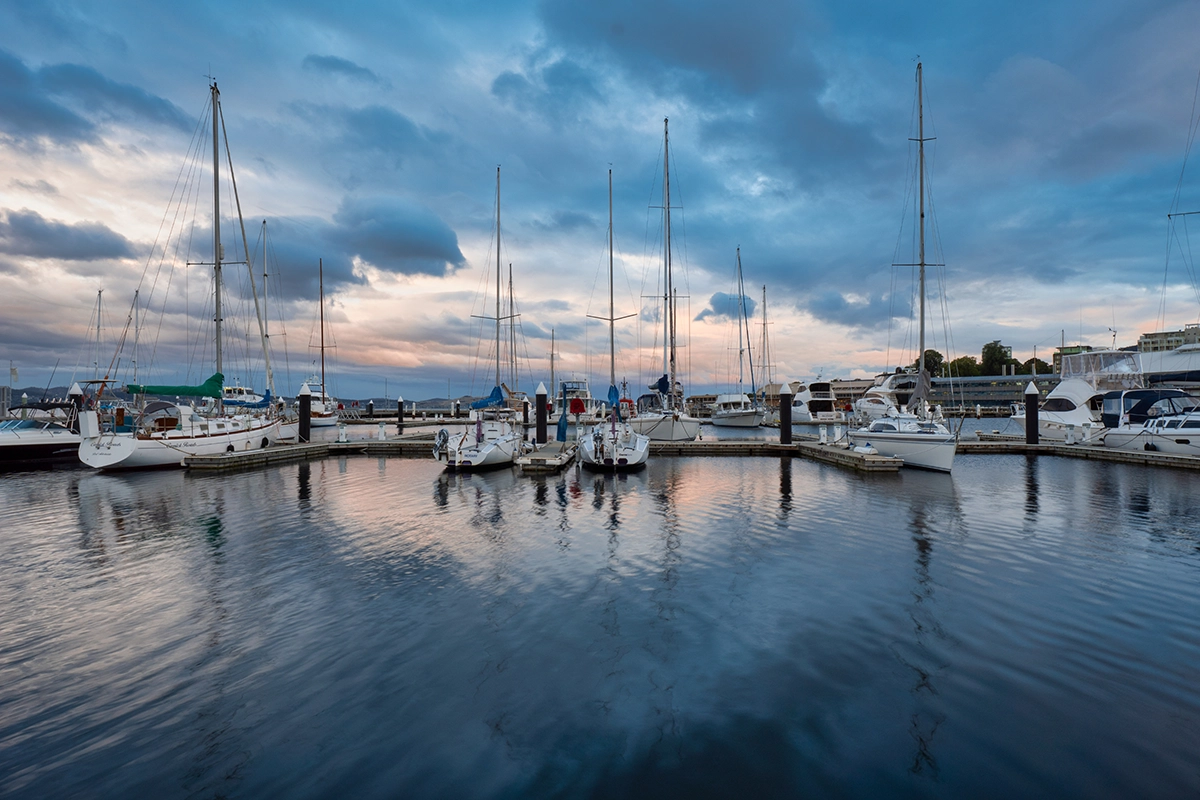 Puerto deportivo con veleros al atardecer reflejándose en aguas tranquilas, capturado en formato de imagen RAW para obtener riqueza de detalles y gama tonal.