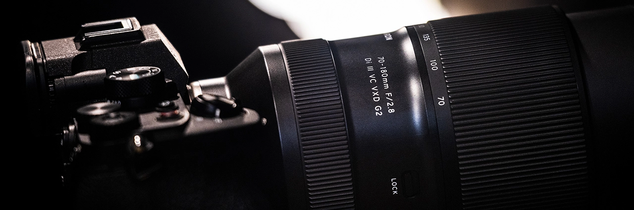 Gros plan sur l'objectif Tamron 70-180mm F/2.8 Di III VC VXD G2 monté sur un appareil photo, mettant en valeur la qualité de fabrication et les performances optiques.